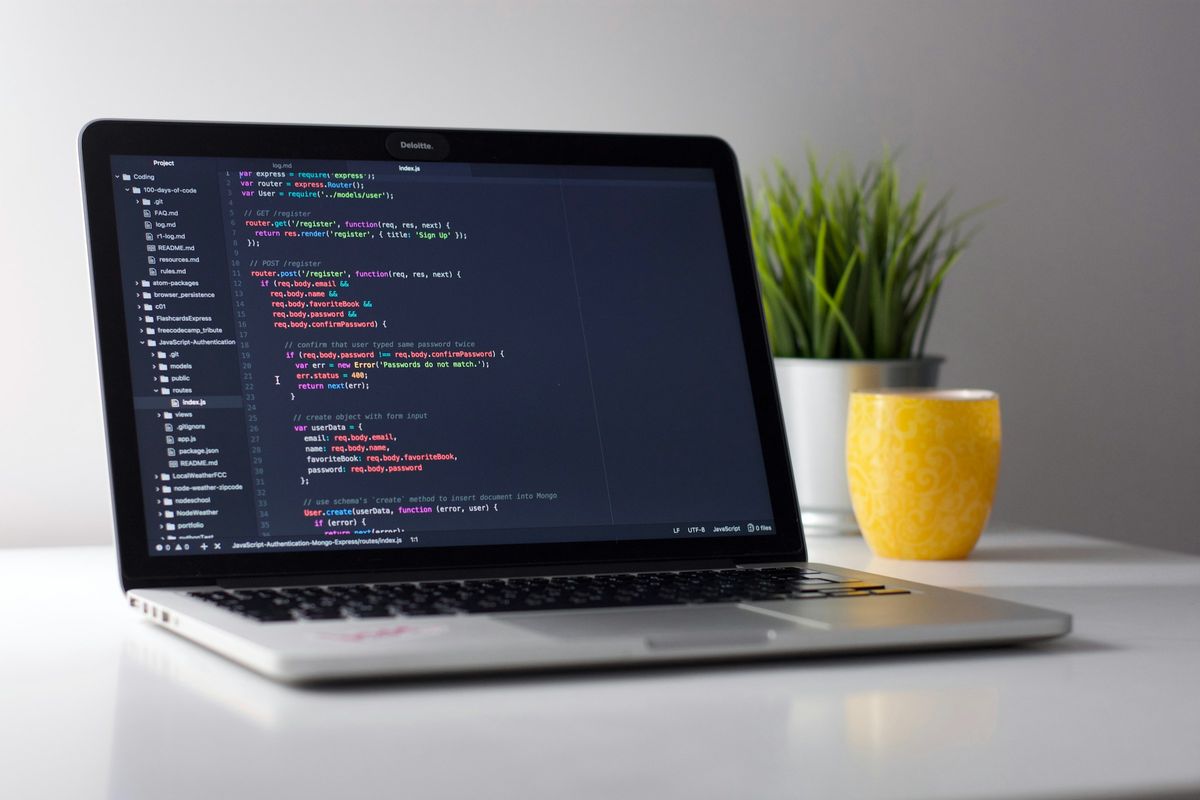 A laptop showing code beside a yellow mug and a plant