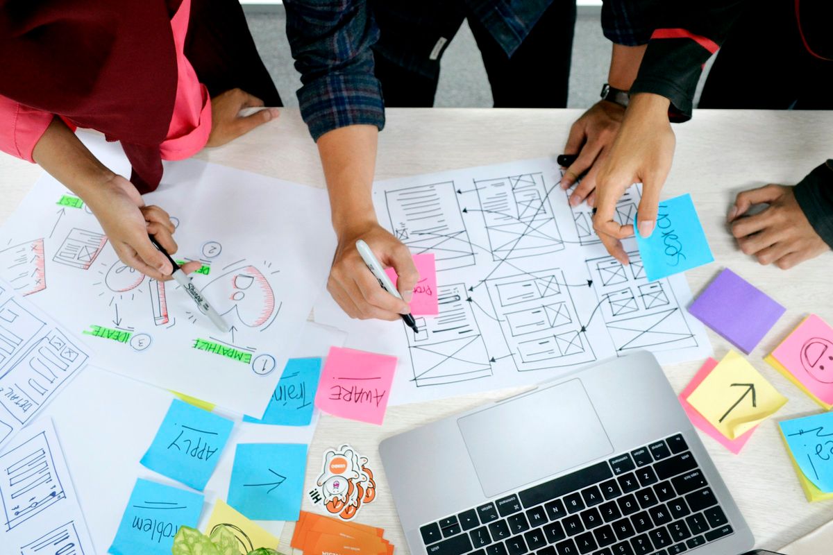 Designers sketching website wireframes with colourful sticky notes and a laptop