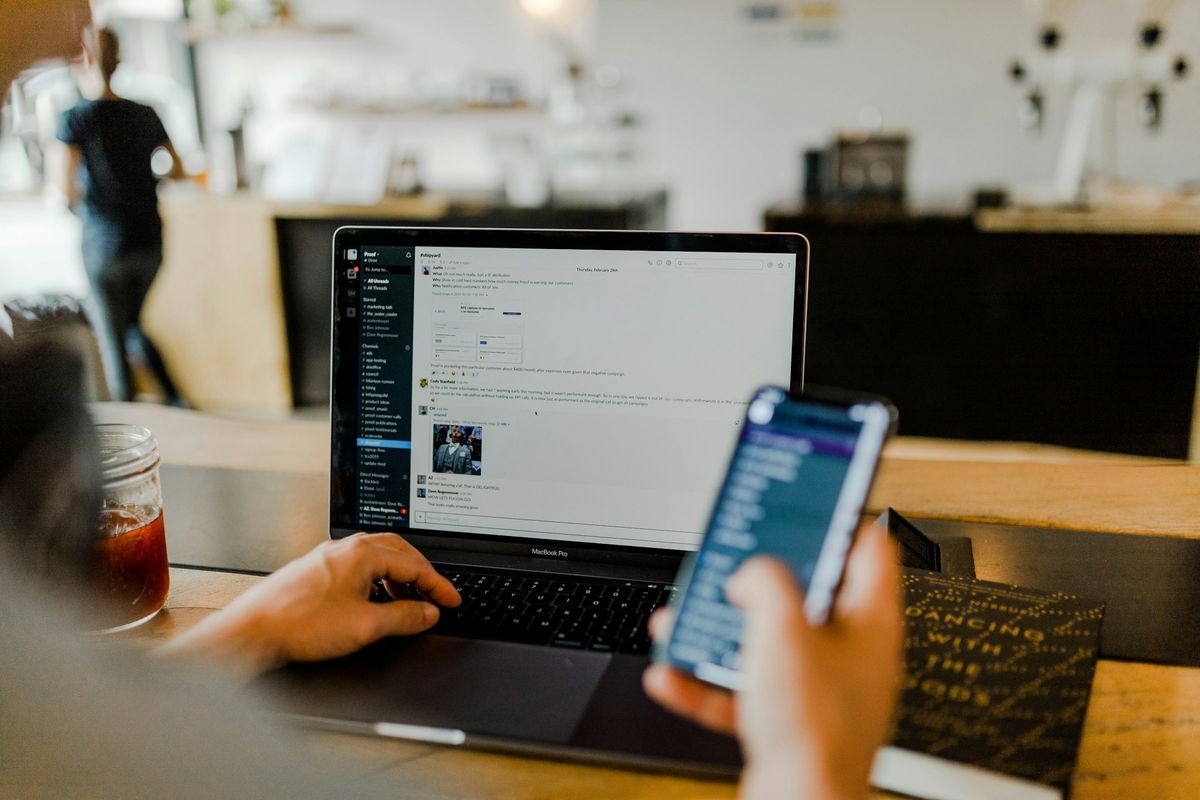 Someone checking a website on their phone and laptop at a wooden desk