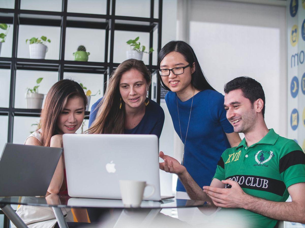A small team gathered round a laptop, smiling at the screen