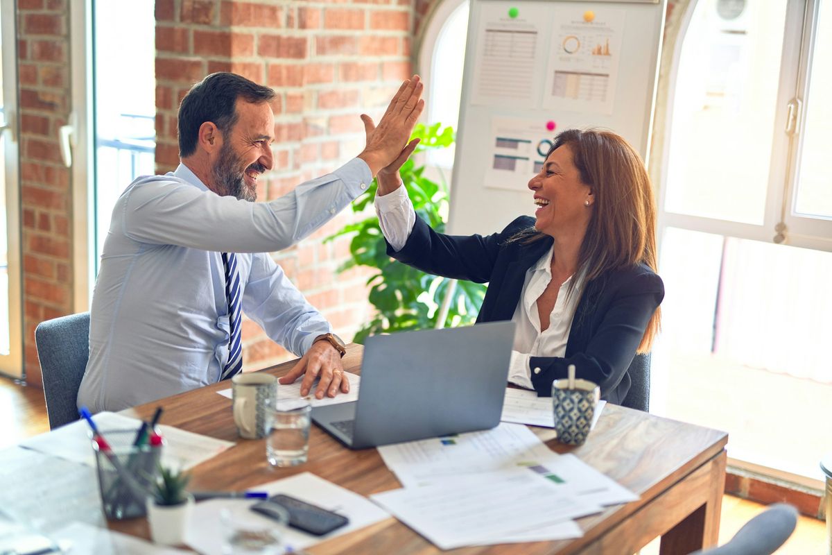 Two colleagues sharing a high five at a sunny office desk
